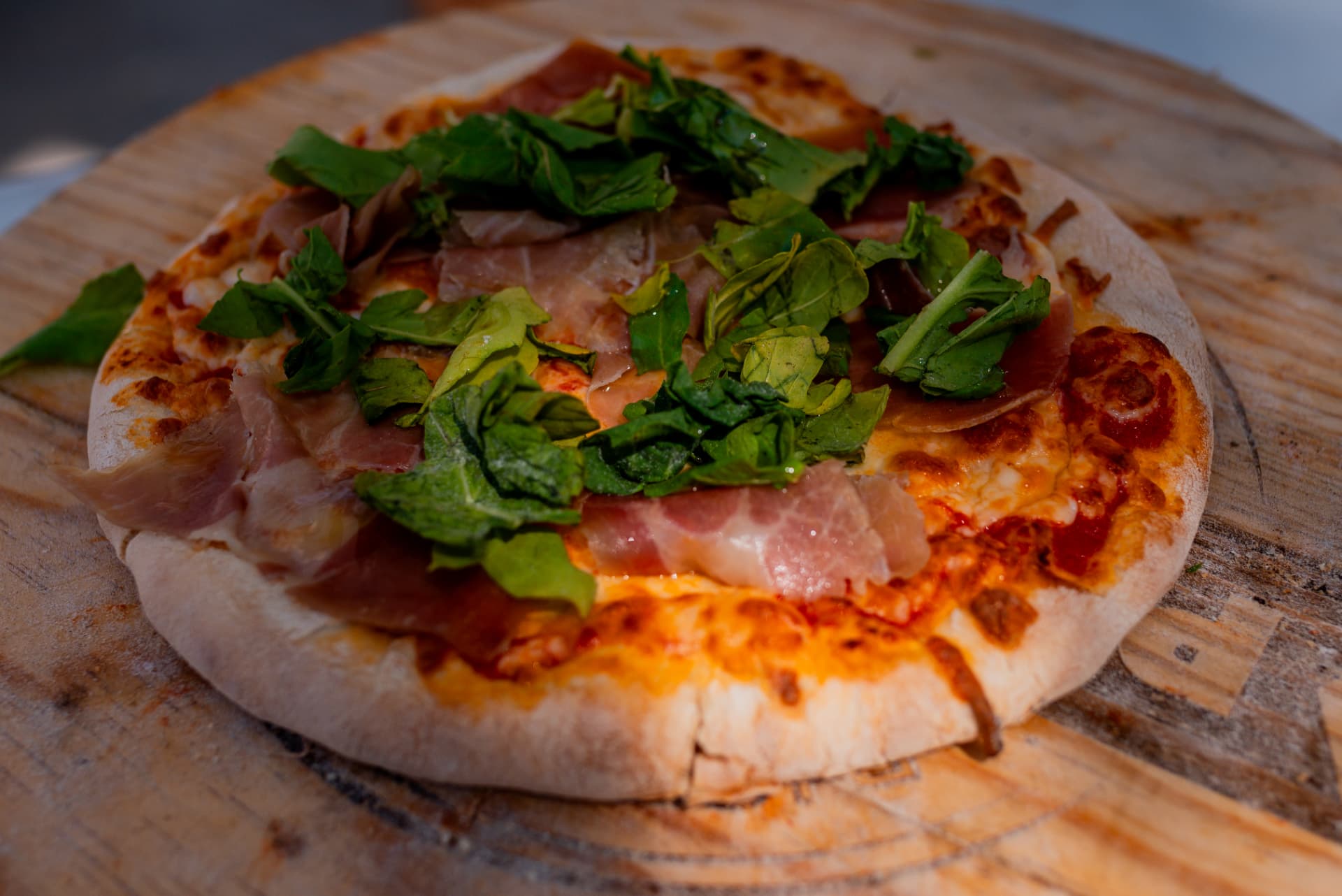 Finished Italiana pizza with prosciutto and arugula on a wooden board